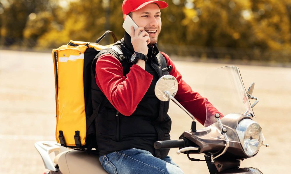 courier-talking-on-mobile-phone-sitting-on-scooter-in-city-1.jpg